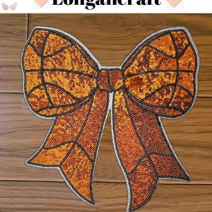 May include: A large, orange sequined bow with a white outline. The bow is on a wooden surface.