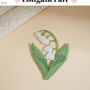 May include: Embroidered lily of the valley patch with white flowers and green leaves. The patch is in the shape of a heart. The text "Longancraft" is above the patch.