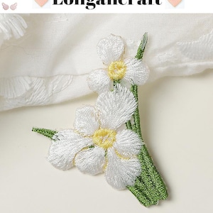 May include: Embroidered white flower applique with yellow centers and green stems. The text "Longancraft" is displayed at the top. The applique is likely for fabric embellishment or craft projects.