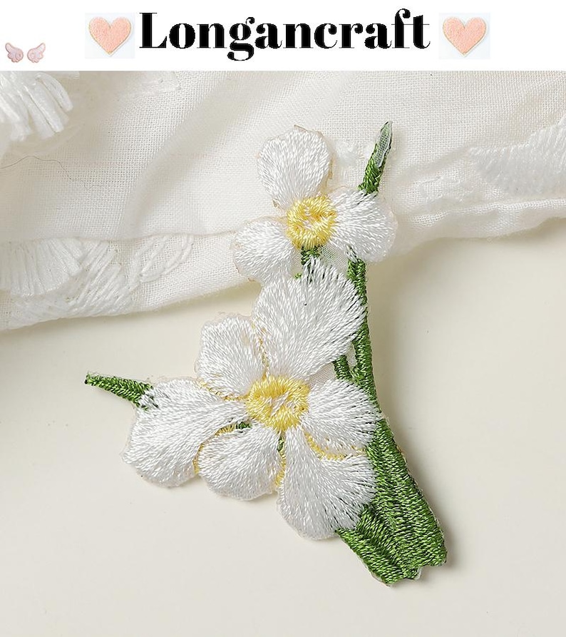 May include: Embroidered white flower applique with yellow centers and green stems. The text "Longancraft" is displayed at the top. The applique is likely for fabric embellishment or craft projects.