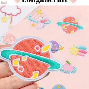 May include: Embroidered patches featuring celestial designs, including planets with rings, stars, and a cloud with hanging stars. The patches are in shades of red, blue, yellow, and pink, with the text "Longancraft" at the top.
