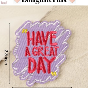 Pode incluir: Etiqueta bordada de ferro de cor roxa com contorno branco. A etiqueta diz "Have a Great Day" em letras cor-de-rosa. A etiqueta tem 2,5 polegadas de largura e 2,8 polegadas de altura.