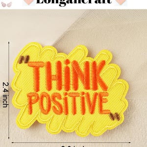 Pode incluir: Etiqueta de ferro bordada amarela com o texto "Think Positive" em letras laranja. A etiqueta mede 7,4 cm de largura e 6,1 cm de altura.