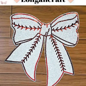 Pode incluir: Um laço branco de lantejoulas com costuras vermelhas e pretas, que se assemelha a uma bola de beisebol. O laço está sobre uma superfície de madeira.