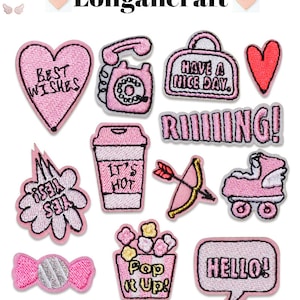 May include: A set of 12 pink and white embroidered iron-on patches with various designs, including a heart with the text "Best Wishes", a phone, a bag with the text "Have a Nice Day", a heart, the text "RIIIIING!" a coffee cup with the text "It's Hot", an arrow, roller skates, a flower with the text "Yes Yes", a candy, a popcorn bucket with the text "Pop It Up!" and a speech bubble with the text "HELLO!"