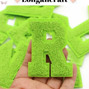 May include: Close-up of a lime green, fuzzy letter "R" patch held in a hand. The patch has a textured, plush appearance. Other green letter patches are in the background. The word "Longancraft" is at the top of the image.