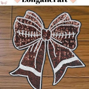 Può includere: Un grande fiocco di paillettes marroni con cuciture bianche e un bordo bianco. Il fiocco è su una superficie di legno.