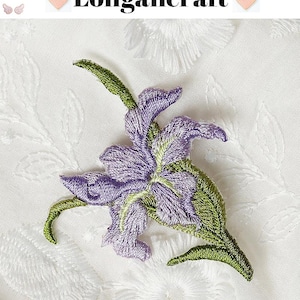 May include: Embroidered purple and green floral applique. The applique features a detailed design of a flower with purple petals and green leaves. The background is white with a subtle floral pattern. The text "Longancraft" is at the top.