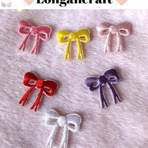May include: Six embroidered iron-on patches in the shape of bows. The bows are in pink, yellow, red, purple, white, and light pink.