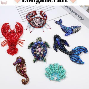 Pode incluir: Conjunto de apliques de criaturas marinhas de contas coloridas, incluindo um lagosta vermelho, uma baleia azul, um peixe azul, um cavalo-marinho roxo, uma tartaruga verde, uma concha azul e um caranguejo vermelho.