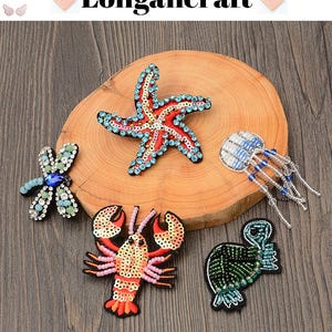 May include: Embroidered patches in various sea-themed designs, including a starfish, dragonfly, jellyfish, lobster, and turtle. The patches are embellished with beads and sequins, and the text "Longancraft" is at the top.