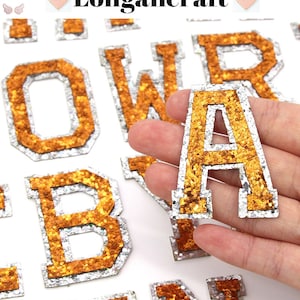 May include: A set of gold glitter iron-on letters with a silver outline. The letters are in uppercase and include the letters O, W, R, A, B, and N. The letters are arranged in a random order on a white background.