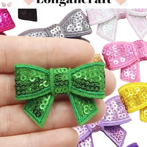 May include: Assortment of green, purple, pink, white, yellow, and gray sequined bows. The bows are made of fabric and have a shiny, sparkly finish.