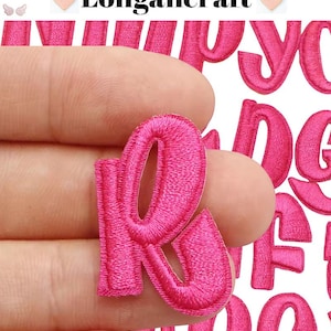 May include: Pink felt letters in various sizes, including the letter R, which is being held by a hand. The letters are ideal for crafting projects.