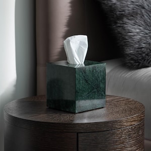 Può includere: Un porta fazzoletti in marmo verde su un comodino in legno scuro con un cassetto. Il porta fazzoletti è accanto a un letto con un cuscino in finta pelliccia grigia.