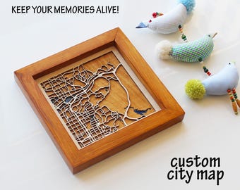 May include: A wooden framed custom city map with a detailed laser-cut design. The map is set against a light-colored background. The text "KEEP YOUR MEMORIES ALIVE!" and "custom city map" are visible. Three decorative bird ornaments are also present.