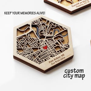 May include: A laser-cut wooden custom city map in a hexagonal shape. The map features a detailed street layout with a red heart marking a location in Ann Arbor, MI. Text includes "KEEP YOUR MEMORIES ALIVE!" and "custom city map."