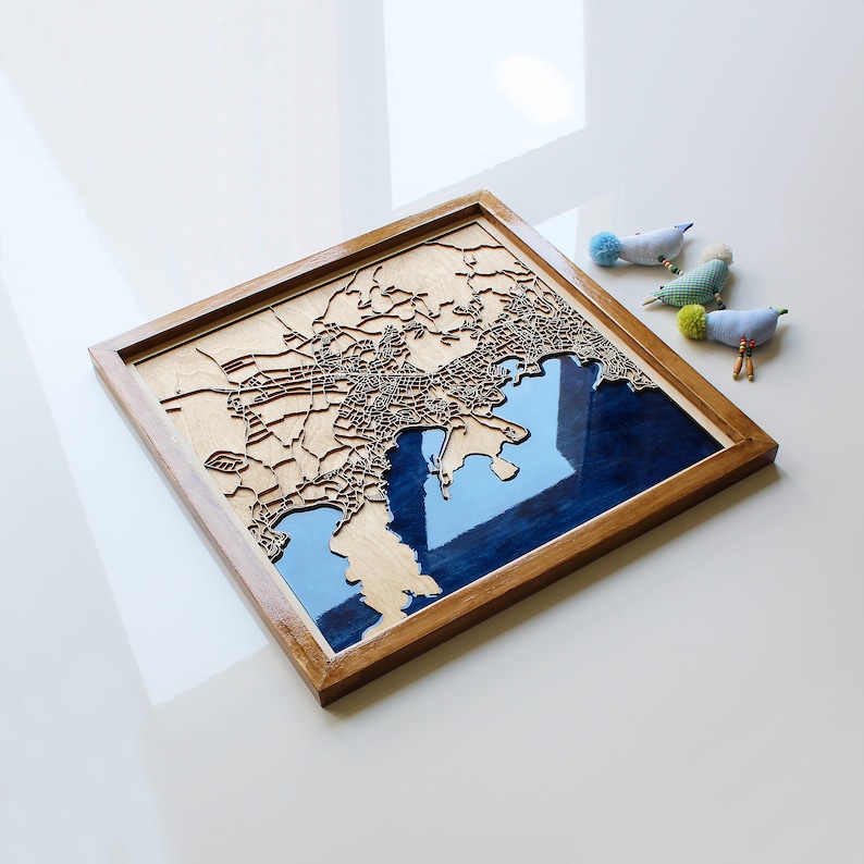 Pode incluir: Um mapa de madeira de uma cidade com uma incrusta&ccedil;&atilde;o de resina azul que representa a &aacute;gua. O mapa &eacute; emoldurado em uma moldura de madeira natural.