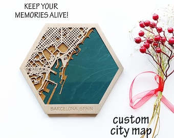 May include: A wooden hexagonal map of Barcelona, Spain, with a teal blue background. The map is laser cut and shows the city streets and coastline. The text "KEEP YOUR MEMORIES ALIVE!" is at the top of the map, and the text "BARCELONA, SPAIN" is at the bottom. The text "custom city map" is written below the map.