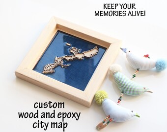 May include: A framed custom wood and epoxy city map with a light wood frame and a blue background. The map is a light brown color. The text "KEEP YOUR MEMORIES ALIVE!" is above the frame. Three fabric bird ornaments are to the right.