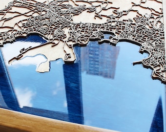 May include: A wooden map of a city with a blue resin inlay, framed in a natural wood frame.