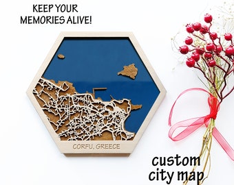 May include: A wooden hexagonal map of Corfu, Greece, with a blue background and white lines representing the city streets. The map is framed in a light wood and has the text "Keep your memories alive!" and "Corfu, Greece" printed on it.