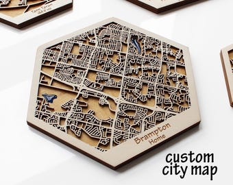 May include: Wooden city map coasters with a laser-cut design. The coasters feature a detailed street layout with blue accents. The text "Brampton Home" and "custom city map" are visible. Other coasters with different city names are also present.
