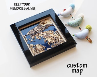 May include: A custom map of a coastal town is framed in black and displayed on a white surface. The map is made of wood and features a blue water body and brown land. The text "KEEP YOUR MEMORIES ALIVE!" is visible above the frame. The words "custom map" are written below the frame.
