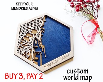 May include: A wooden hexagonal map of Barcelona, Spain, with a detailed laser-cut city plan over a blue background. The text "KEEP YOUR MEMORIES ALIVE!" is above the map. The words "custom world map" are below the map.