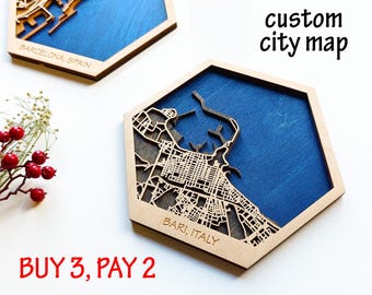 May include: Two wooden city map artworks, one labeled "Barcelona, Spain" and the other "Bari, Italy." Each map is laser-cut with intricate street details and set against a blue background. The text "custom city map" is also visible.