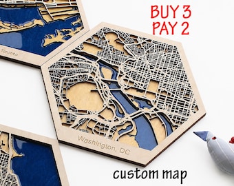 May include: Hexagonal wooden wall art featuring a layered 3D map of Washington, DC, with blue water details and natural wood street grids. The text reads BUY 3 PAY 2 and custom map. The piece includes a laser-cut design with visible depth.
