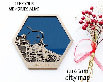 May include: A wooden hexagonal map of Bari, Italy, with a blue background and the text "Keep your memories alive!" and "Bari, Italy". The map is on a white surface with a red ribbon and a bouquet of red berries.