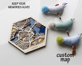 May include: A wooden hexagonal map of Boston with a blue water feature. The map is surrounded by three small, colorful, fabric birds with pom-poms. The text "KEEP YOUR MEMORIES ALIVE!" is at the top of the image. The text "custom map" is at the bottom of the image.