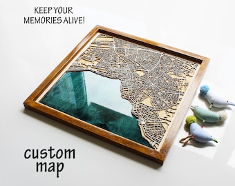 May include: A wooden map of a city with a teal blue resin inlay, framed in a dark wood frame. The text "KEEP YOUR MEMORIES ALIVE!" is above the map and the text "custom map" is below the map.