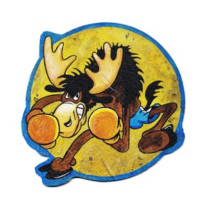 Può includere: Un alce dei cartoni animati che indossa guantoni da boxe e pantaloncini blu, su uno sfondo giallo con un bordo blu.