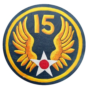 Peut inclure: Un écusson rond bleu et jaune avec une étoile blanche et un centre rouge. L'étoile est entourée de deux ailes jaunes. Le numéro "15" est au centre de l'écusson.