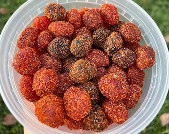 May include: A clear plastic container filled with red and black gummy candies. The candies are covered in a red and black sugar coating.