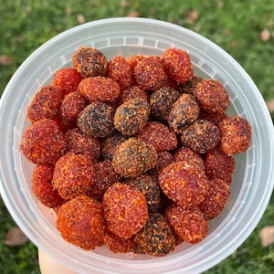 Puede incluir: Un recipiente de plástico transparente lleno de caramelos gomosos rojos y negros. Los caramelos están cubiertos con una capa de azúcar roja y negra.