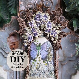 Op de afbeelding: Een decoratief doe-het-zelf kunstwerk met een fles met een vlinderontwerp, versierd met paarse bloemen en een golfkartonnen frame. De tekst "DOWNLOAD INSTRUCTIE DIY Design by Gea Veldhuis" is zichtbaar.