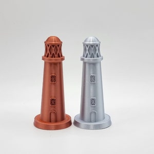 May include: Two miniature lighthouses, one is copper coloured and the other is silver. Both have a white base and a black window.