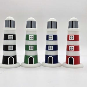 May include: Four decorative lighthouse ornaments in black, green, blue, and red with white details. Each lighthouse has a white top, a black and grey lantern, and a white base. The lighthouses have a striped design and small square windows.