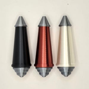 May include: Three decorative bottle stoppers in black, red, and off-white. Each stopper has a conical shape with a grey top and a decorative base. The stoppers are designed to fit into a bottle opening.