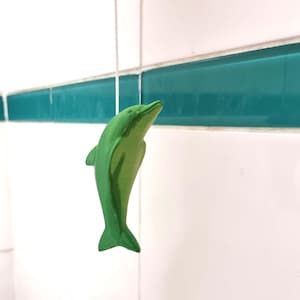 May include: A green dolphin figurine hanging from a string in a bathroom with white and teal tiles.