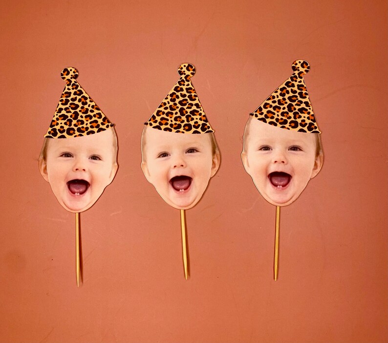 May include: Three cake toppers featuring a child's face with a leopard print party hat. Each topper is on a wooden stick.
