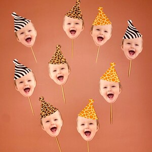 May include: Nine cupcake toppers featuring different animal print party hats with a baby's face in each hat. The hats are in various animal prints, including zebra, giraffe, and leopard.