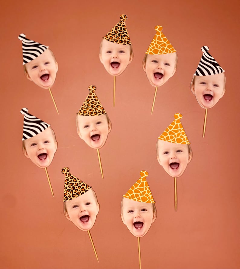 May include: Nine cupcake toppers featuring different animal print party hats with a baby's face in each hat. The hats are in various animal prints, including zebra, giraffe, and leopard.
