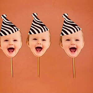 May include: Three black and white striped party hats with a child's face in each. The faces are smiling and have their mouths open. The hats are on sticks.