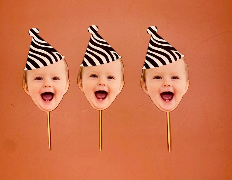 May include: Three black and white striped party hats with a child's face in each. The faces are smiling and have their mouths open. The hats are on sticks.