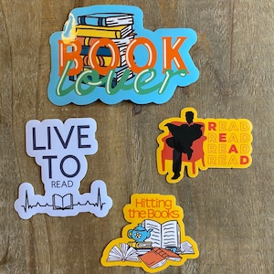 May include: Four colorful stickers with book-themed designs. The first sticker is blue with a stack of books and the text "BOOK lover". The second sticker is white with the text "LIVE TO READ" and a heart rate line with a book icon. The third sticker is yellow with the text "Hitting the Books" and an illustration of a book, a teacup, and other books. The fourth sticker is yellow with a silhouette of a person sitting in a chair and the text "READ READ READ READ".
