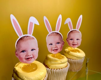 May include: Three yellow cupcakes with white frosting and a clear jelly center. Each cupcake has a bunny ear headband with a baby's face in the center.
